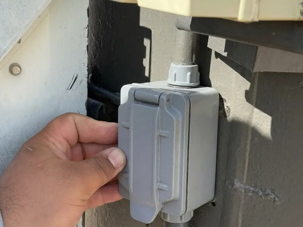 Sample after photo: the same outdoor box with a gray weatherproof cover on, wires hidden, a hand resting beside it.