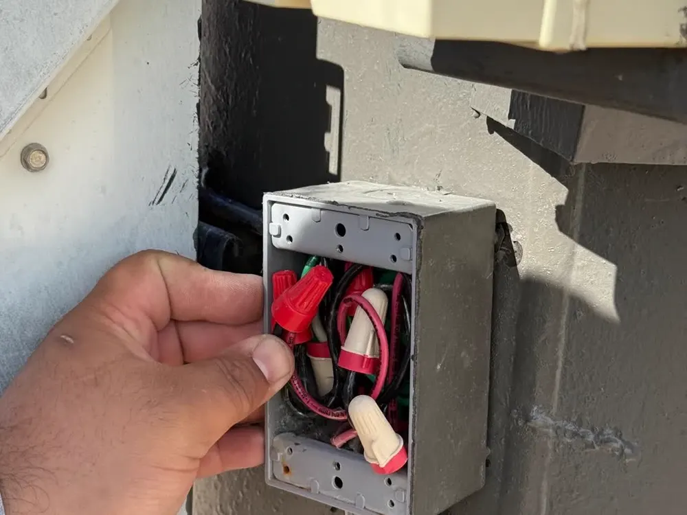 Before photo: an outdoor metal box with the cover off and loose red wire nuts and wires showing, a hand holding it.