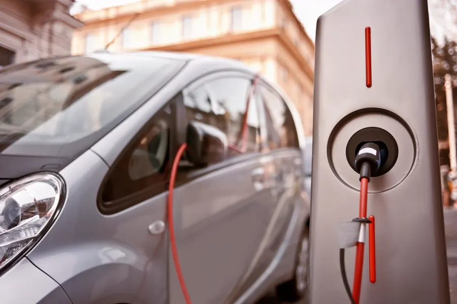 Stock photo: a red electric car plugged into a wall charger in a concrete garage.