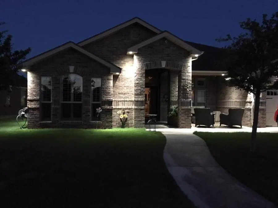 A brick house at night with lights washing up the walls and a lit path to the front door.