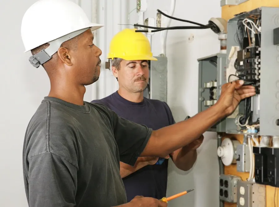 Stock photo: two electricians in hard hats working at an open electrical panel.